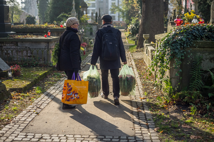 A couple carries plastic bags full of flowers across the cemetery, All Saints' Day in Poland. Image: Michel Meijer