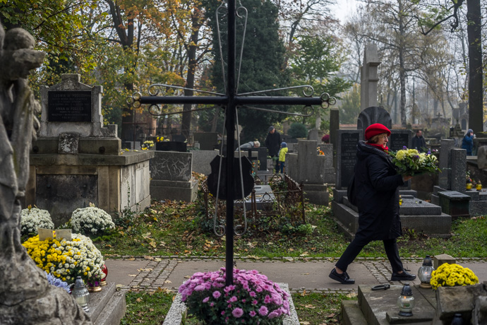 A woman with a red hat and a bouquet of flowers in her hands is walking through the cemetery, All Saints' Day in Poland. Image: Michel Meijer
