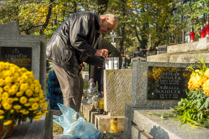 A man lights a number of candles on a tombstone, All Saints' Day in Poland. Image: Michel Meijer