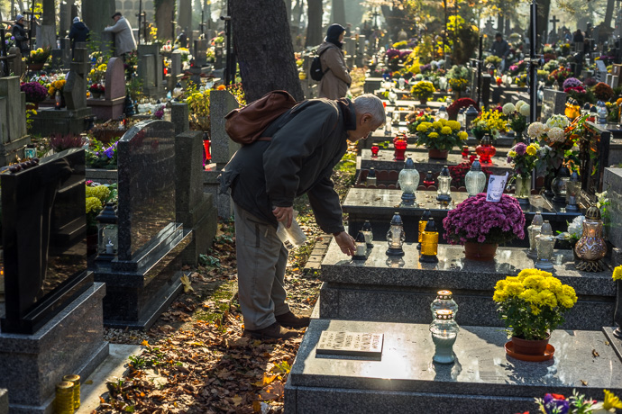 A man puts a candle on a tombstone, All Saints' Day in Poland. Image: Michel Meijer