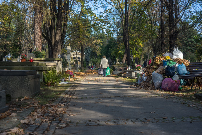 A woman walks through the cemetery with a trolley and a green plastic bag in her hand, All Saints' Day in Poland. Image: Michel Meijer
