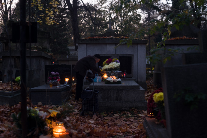 An old woman places flowers and candles on a tombstone, All Saints' Day in Poland. Image: Michel Meijer