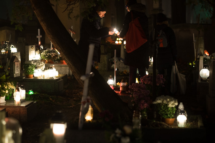 People light candles above a grave stone in a cemetery, All Saints' Day in Poland. Image: Michel Meijer